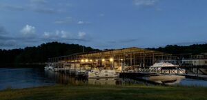 Illuminated boat slips and docks under a covered marina at dusk.